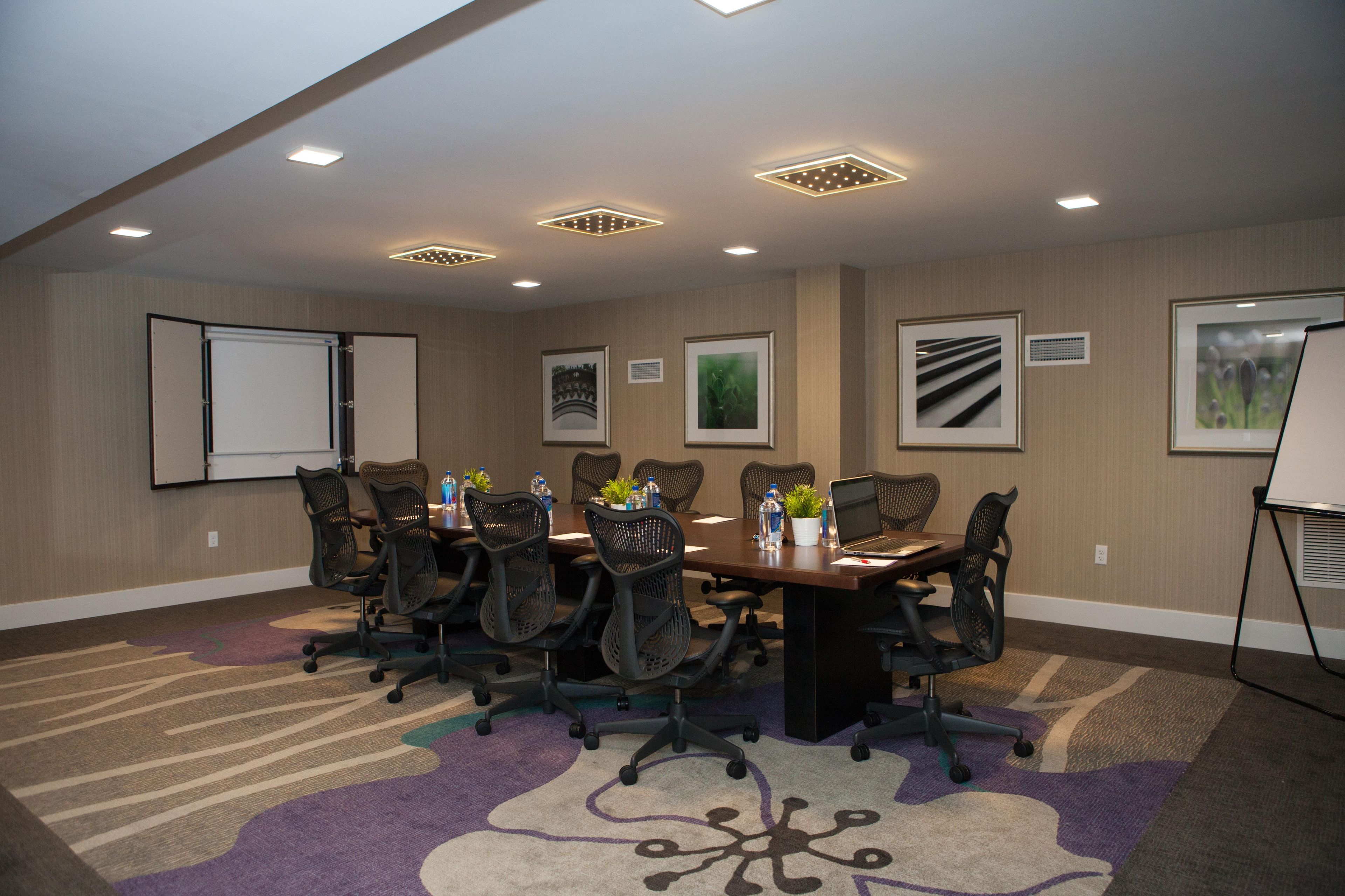 Una sala de conferències amb una taula llarga, diverses cadires, una pantalla de projector i quadres a les parets.