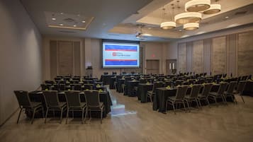 Une salle de conférence dotée de plusieurs tables et chaises, d’un grand écran diffusant une présentation et d’un design de plafond moderne.