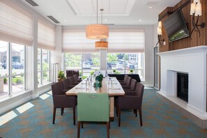 A conference room with a long table, chairs, a fireplace, and large windows. - Hilton Garden Inn Springfield (Springfield)