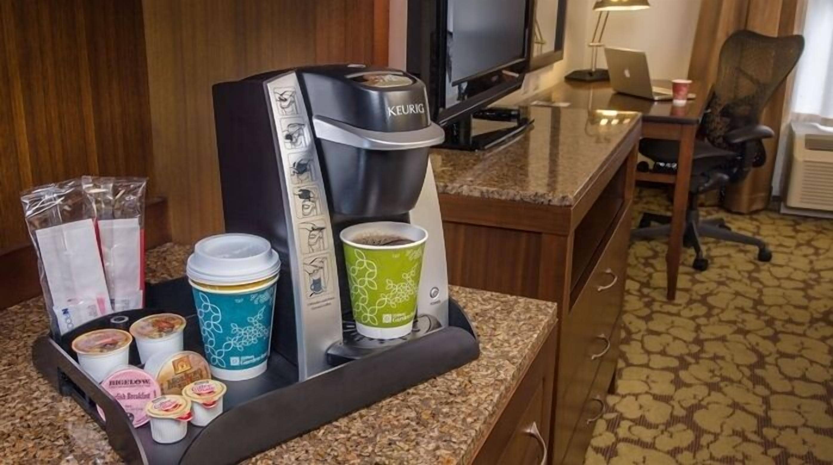 A coffee station with a Keurig machine, disposable cups, and food items like yogurt and granola.
