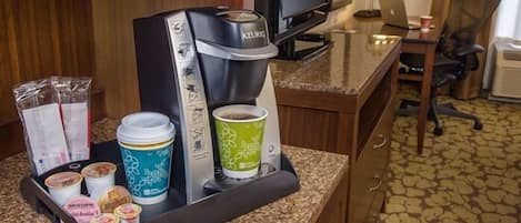 A coffee station with a Keurig machine, disposable cups, and food items like yogurt and granola.