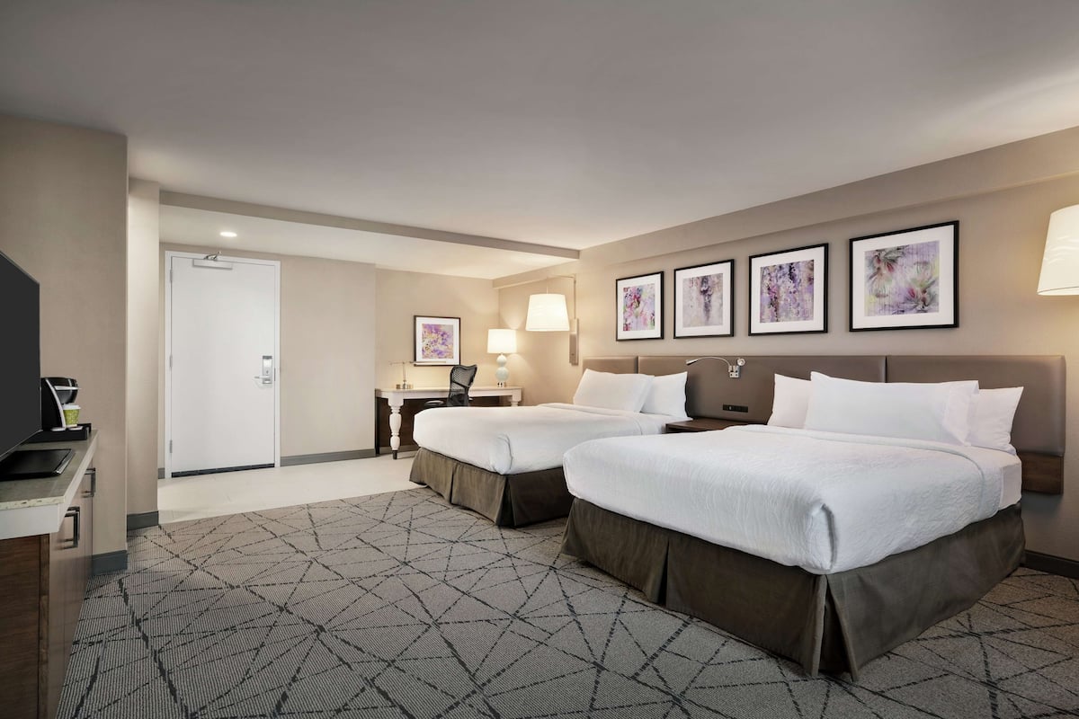 A hotel room with two beds, a desk, a chair, and a TV.
