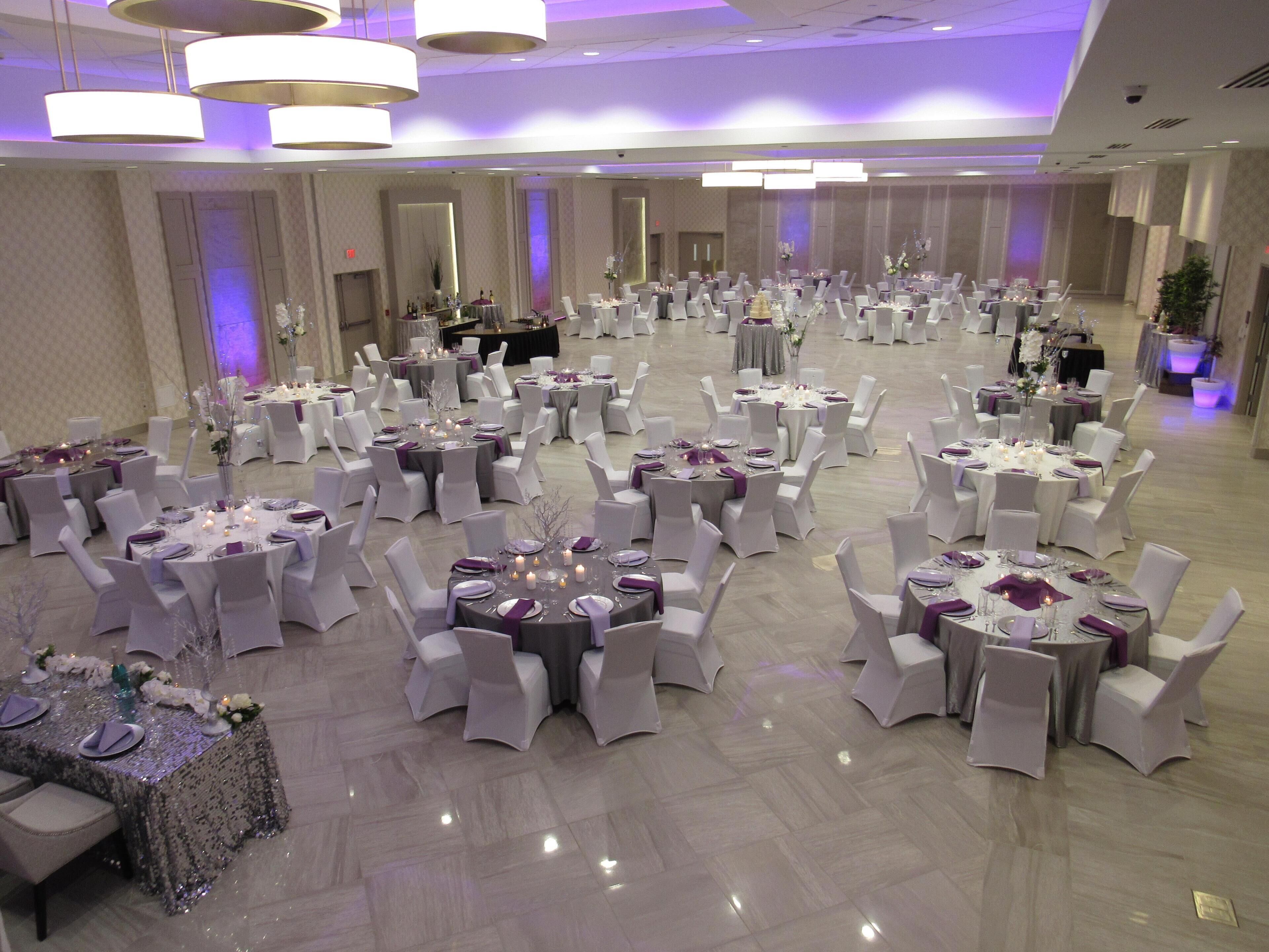 A large banquet hall with round tables, white chairs, and purple accents.