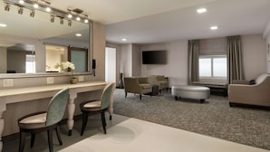 A hotel room with a vanity area, two armchairs, a sofa, and a flat-screen TV.