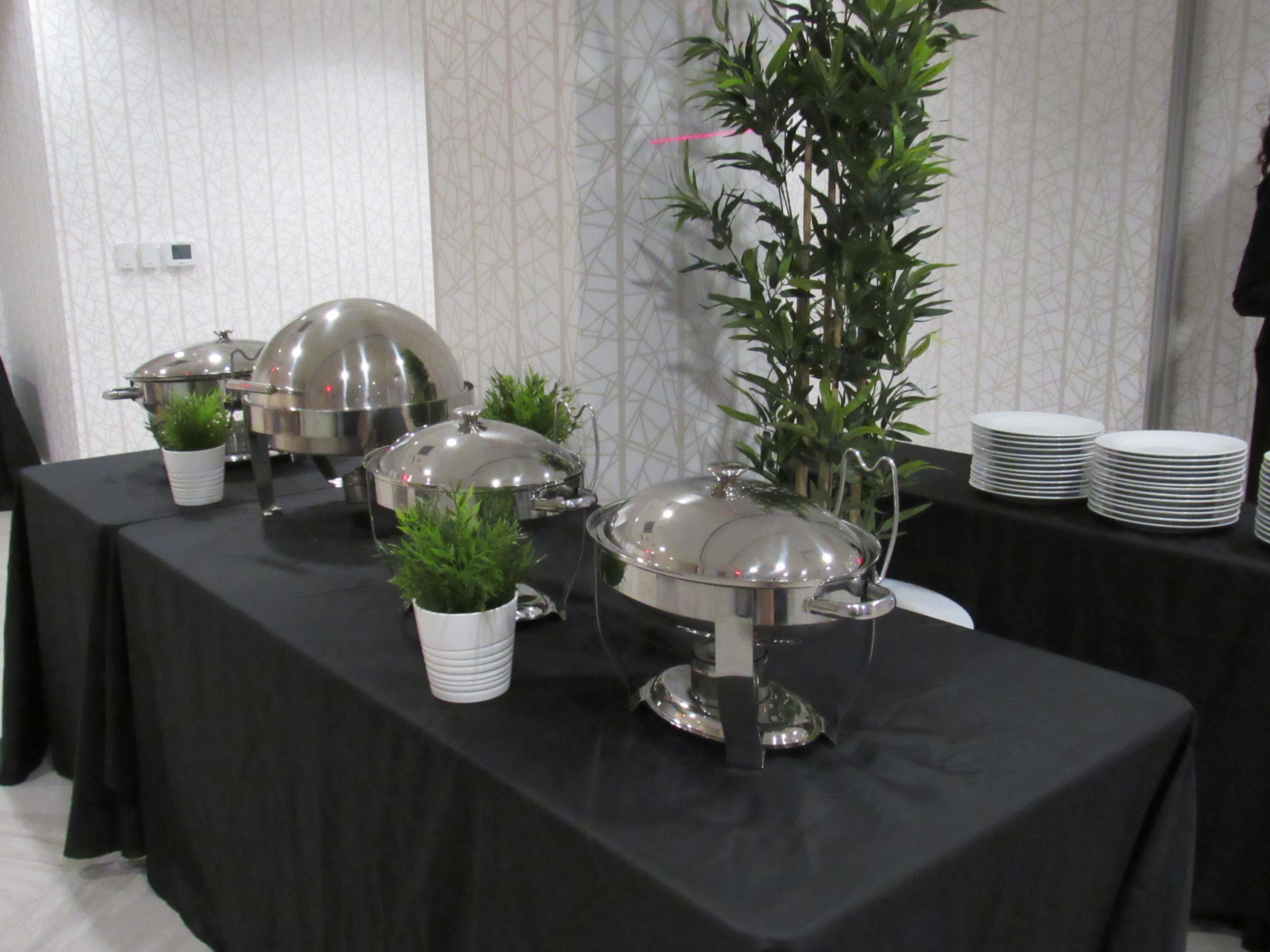 A buffet setup with covered food stations and a potted plant.