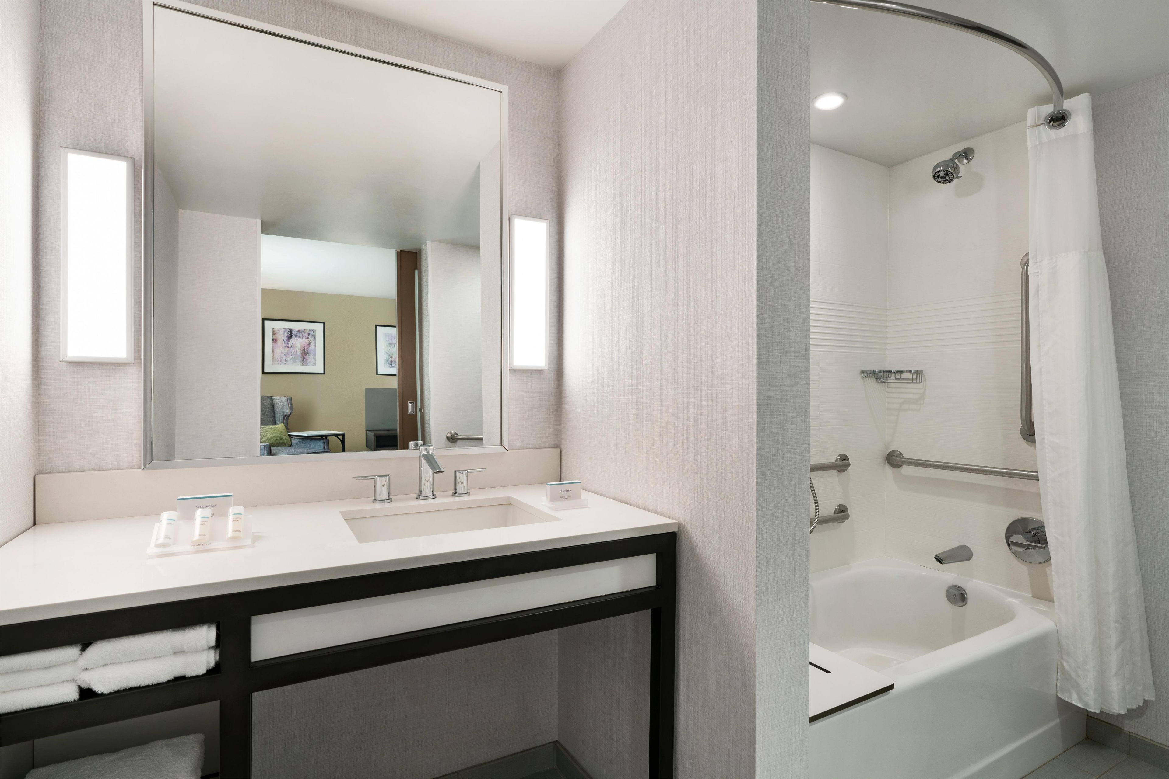 A modern bathroom with a white sink, a mirror, a shower with a curved glass door, and a towel rack.