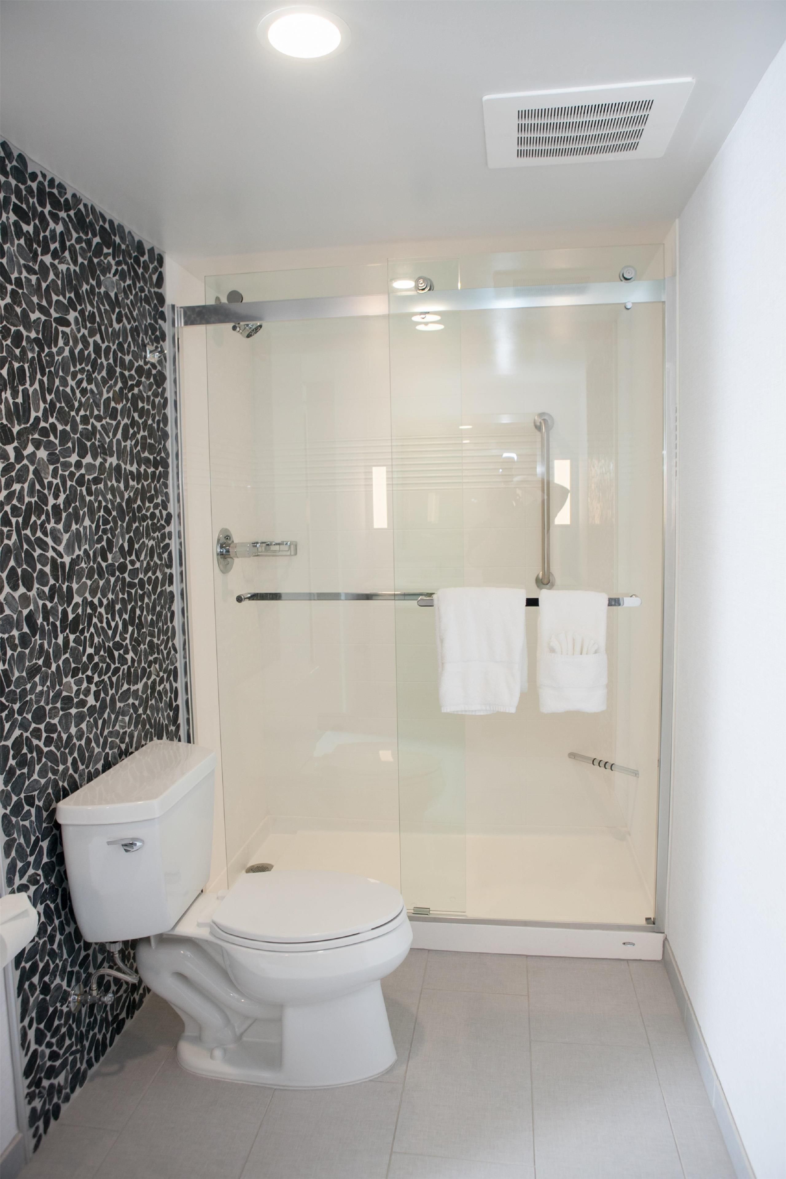Un bagno moderno con cabina doccia in vetro, un water bianco e una parete con decoro in pietra.