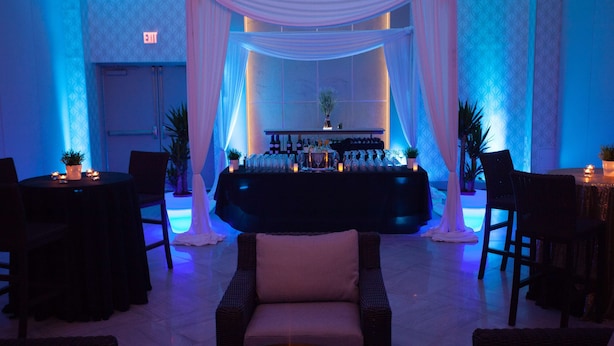 A bar area with a black tablecloth, white drapes, and a variety of bottles and glasses.