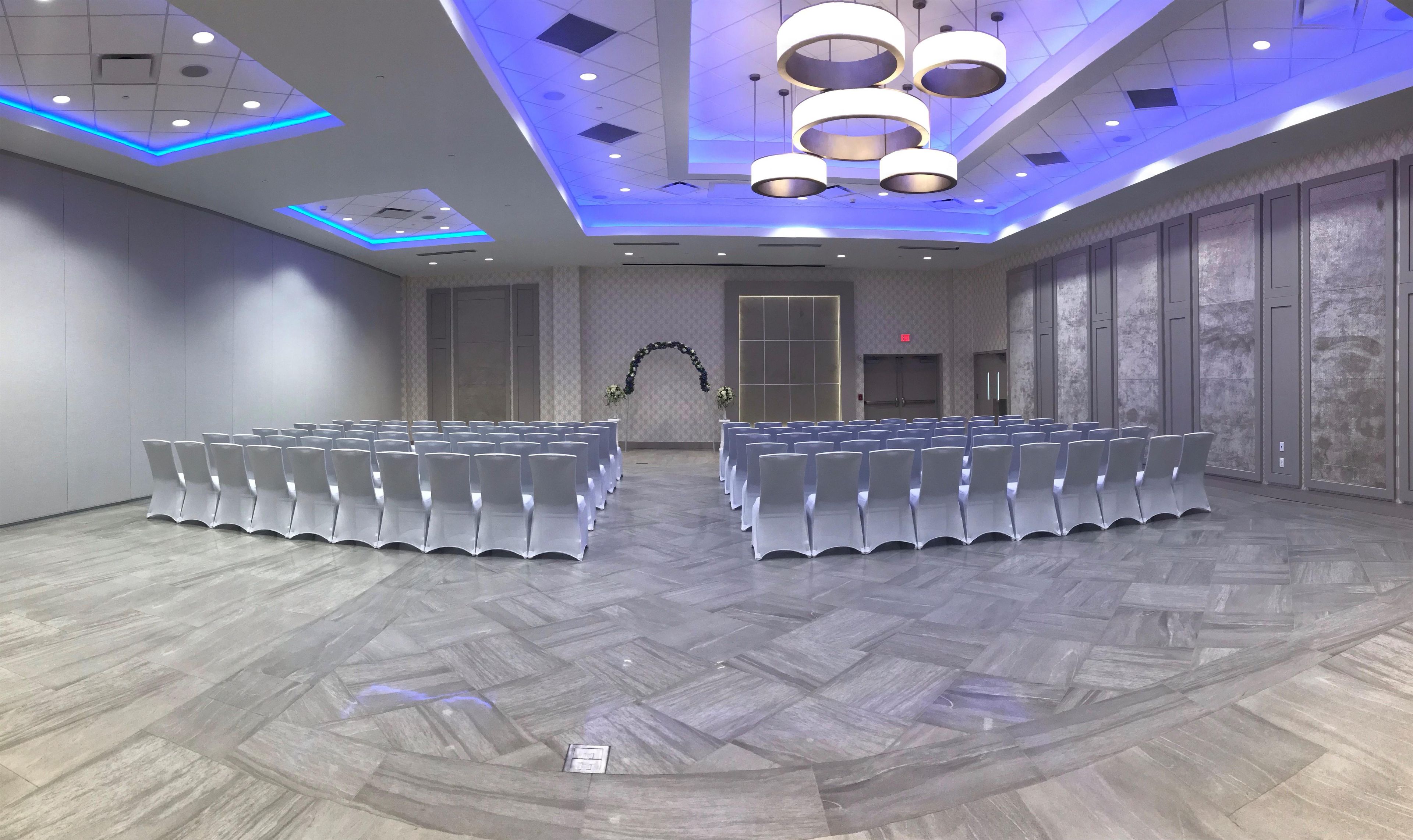 A conference room with rows of white chairs, a decorative arch, and modern lighting fixtures.