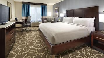 A hotel room with a large bed, a desk with a chair, a television, and a window with curtains.