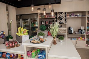 A well-organized snack bar with various packaged snacks, a refrigerator stocked with beverages, and a coffee machine. - Hilton Garden Inn Springfield (Springfield)