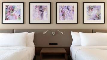 A hotel room with two beds, a nightstand, and four framed floral artworks on the wall.