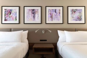 A hotel room with two beds, a nightstand, and four framed floral artworks on the wall.