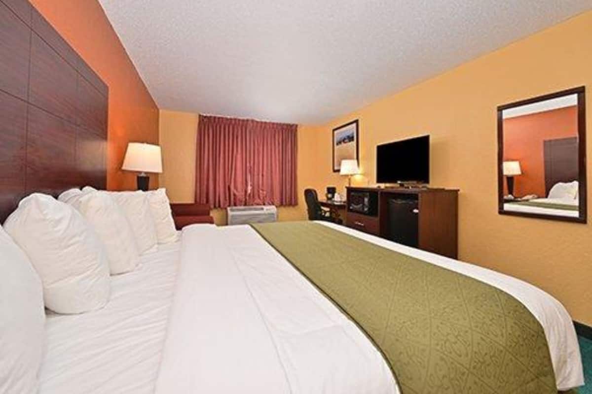 Une chambre d’hôtel avec un grand lit, un bureau avec un ordinateur, un téléviseur à écran plat et une fenêtre avec des rideaux.
