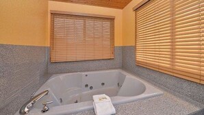 A bathroom with a freestanding bathtub, wooden ceiling, and blinds on the windows.