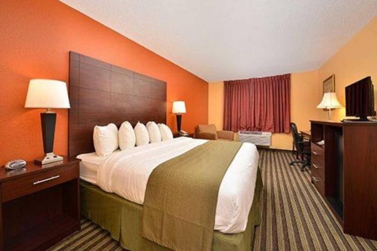 Une chambre d’hôtel avec un grand lit, deux tables de chevet avec des lampes, un bureau, une chaise et une fenêtre avec des rideaux.
