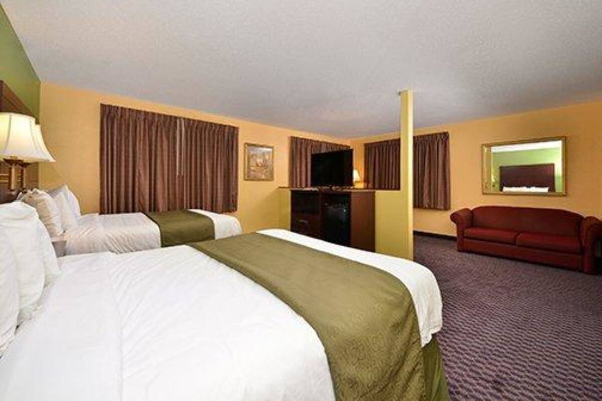 Une chambre d’hôtel avec deux lits, une télévision, un canapé et un sol recouvert de moquette.