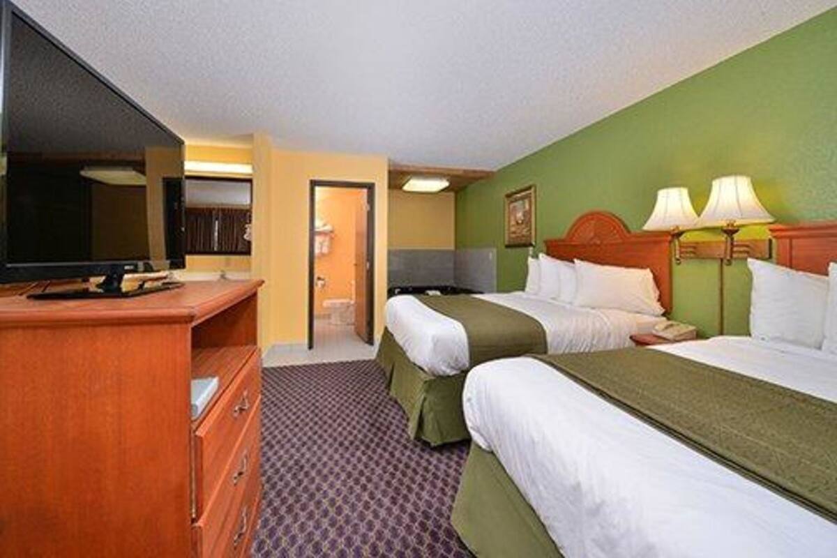 Une chambre d’hôtel avec deux lits, une télévision, un bureau et une porte donnant sur une salle de bain.