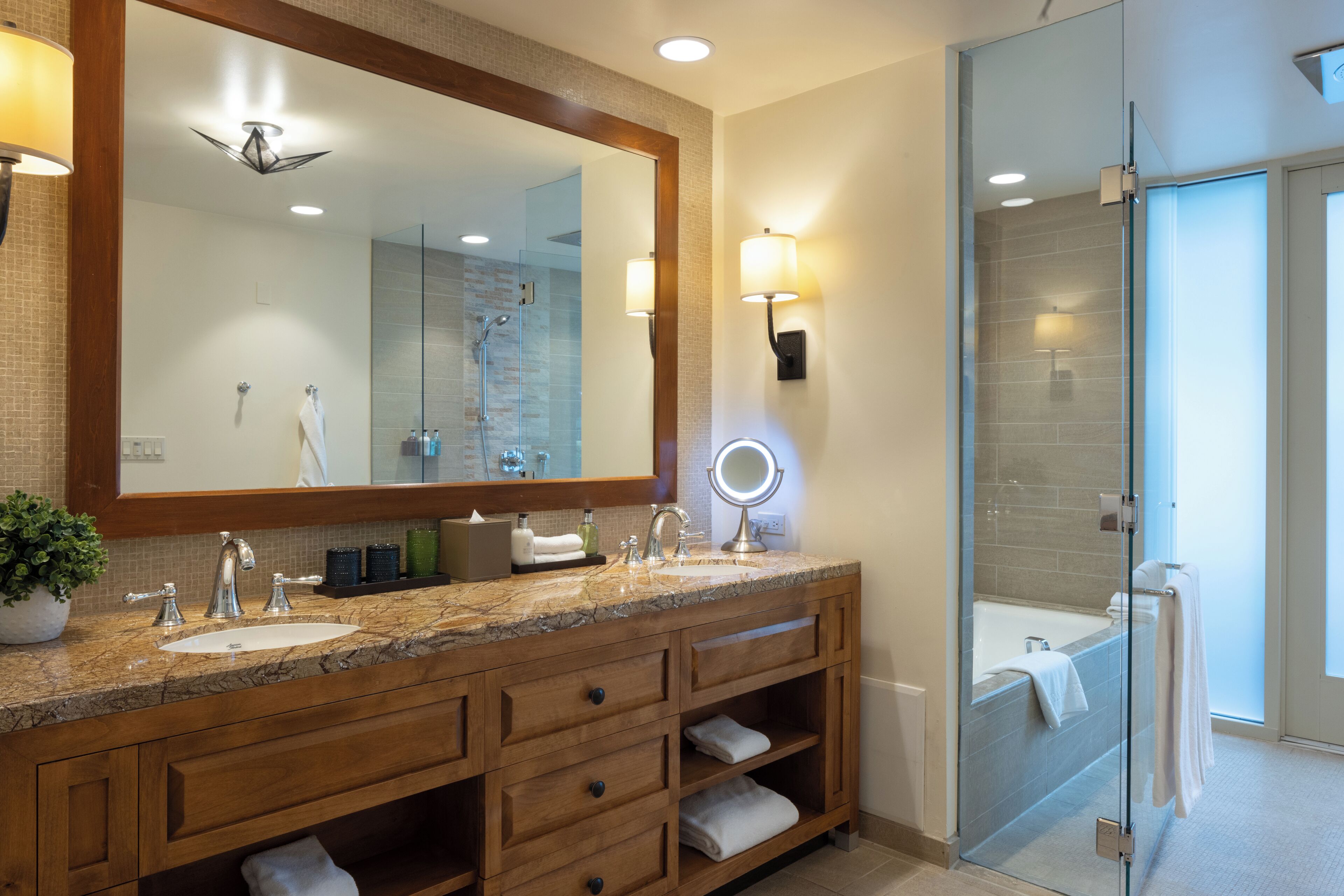Een moderne badkamer met een grote spiegel, dubbele wastafels, een douche met glazen wand en ingebouwde planken.