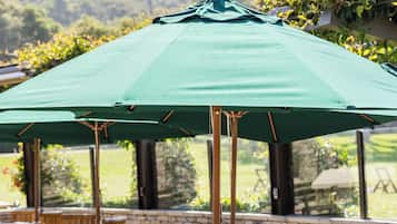 An outdoor patio area with wooden tables and chairs, a green umbrella, and a stone wall.