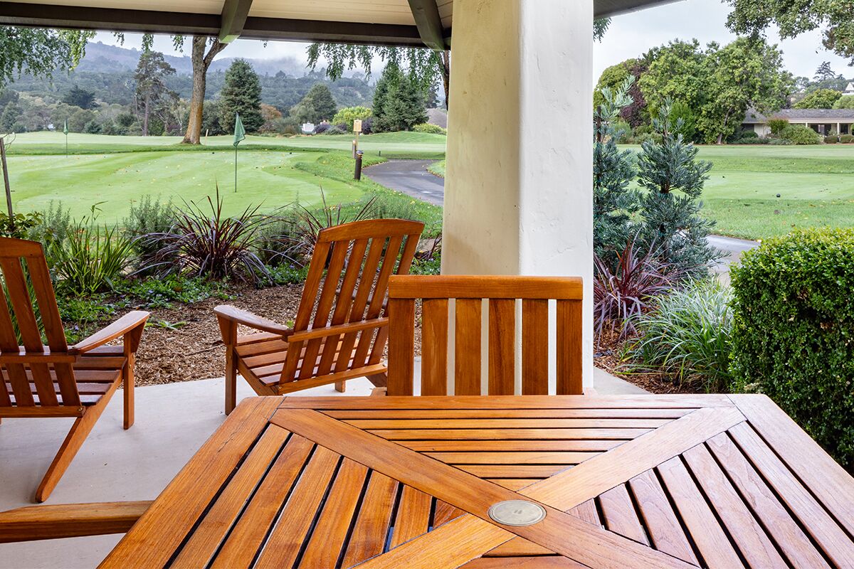 Una mesa y sillas de madera en un patio con vistas a un campo de golf.