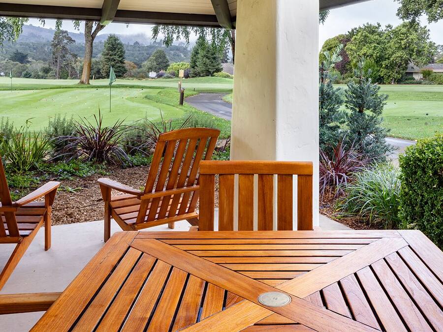 Una mesa y sillas de madera en un patio con vistas a un campo de golf.