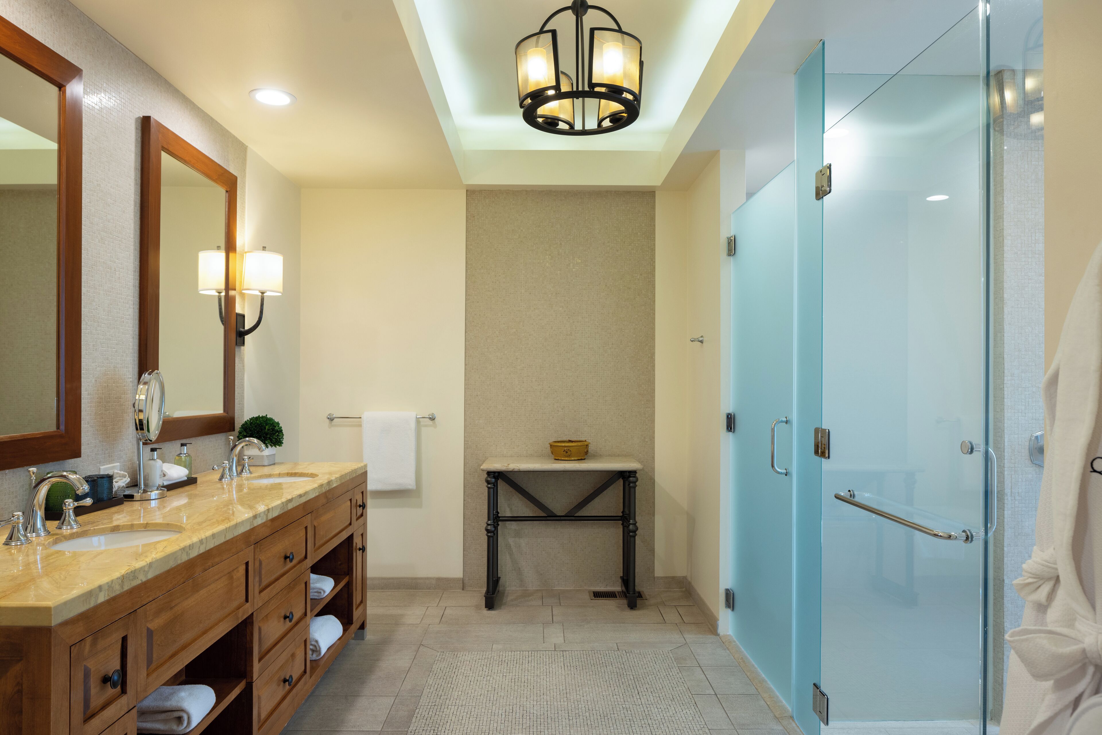 A bathroom with two sinks, a vanity, a mirror, a shower, and a ceiling light.