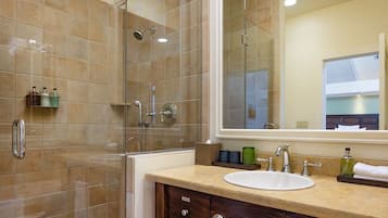 A modern bathroom with a glass-enclosed shower, a sink with a mirror above it, and toiletries on the counter.