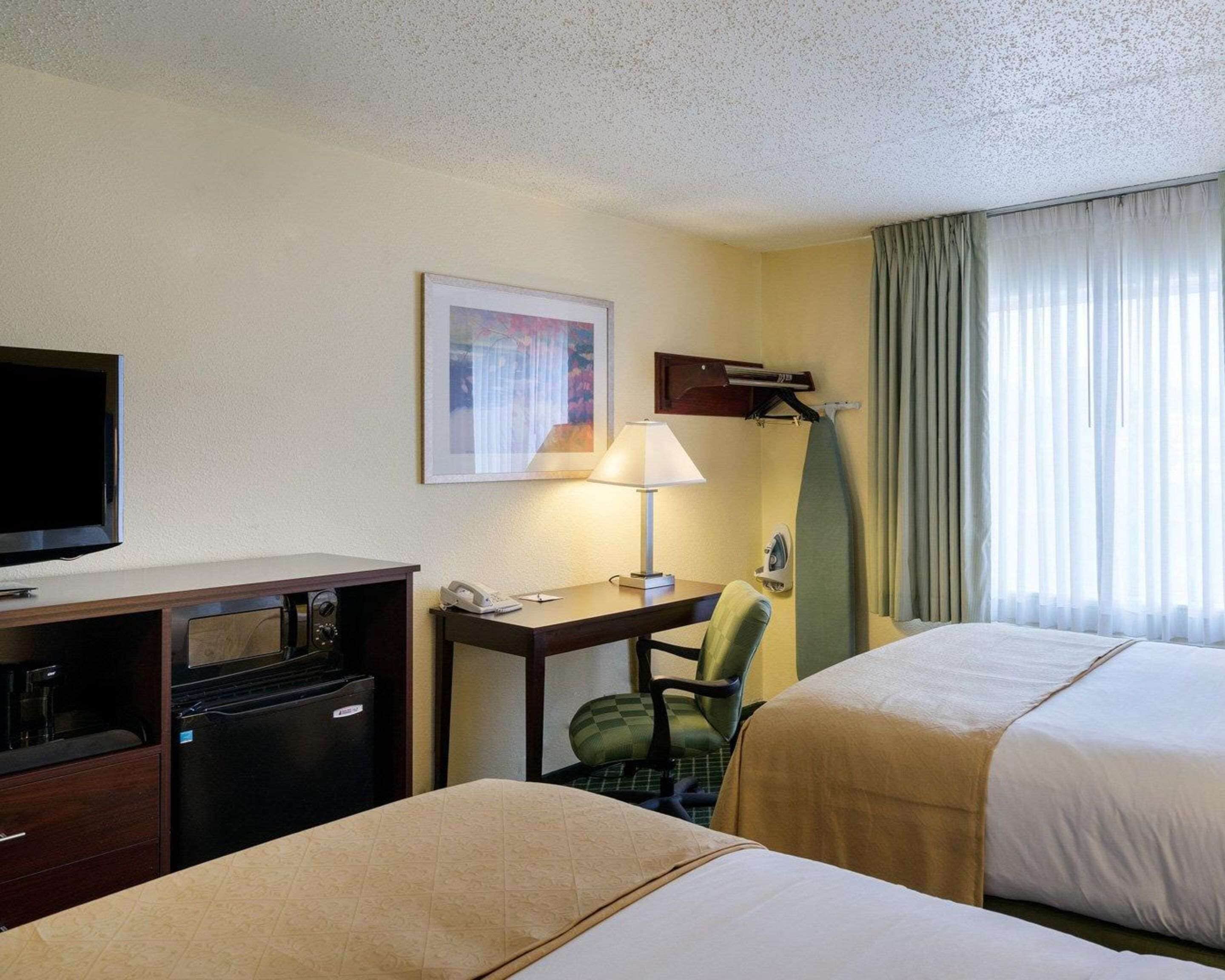 Une chambre d’hôtel avec deux lits, un bureau avec une lampe, une télévision, un minibar et une fenêtre avec des rideaux.
