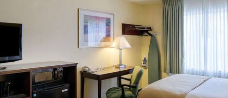 Une chambre d’hôtel avec deux lits, un bureau avec une lampe, une télévision, un minibar et une fenêtre avec des rideaux.