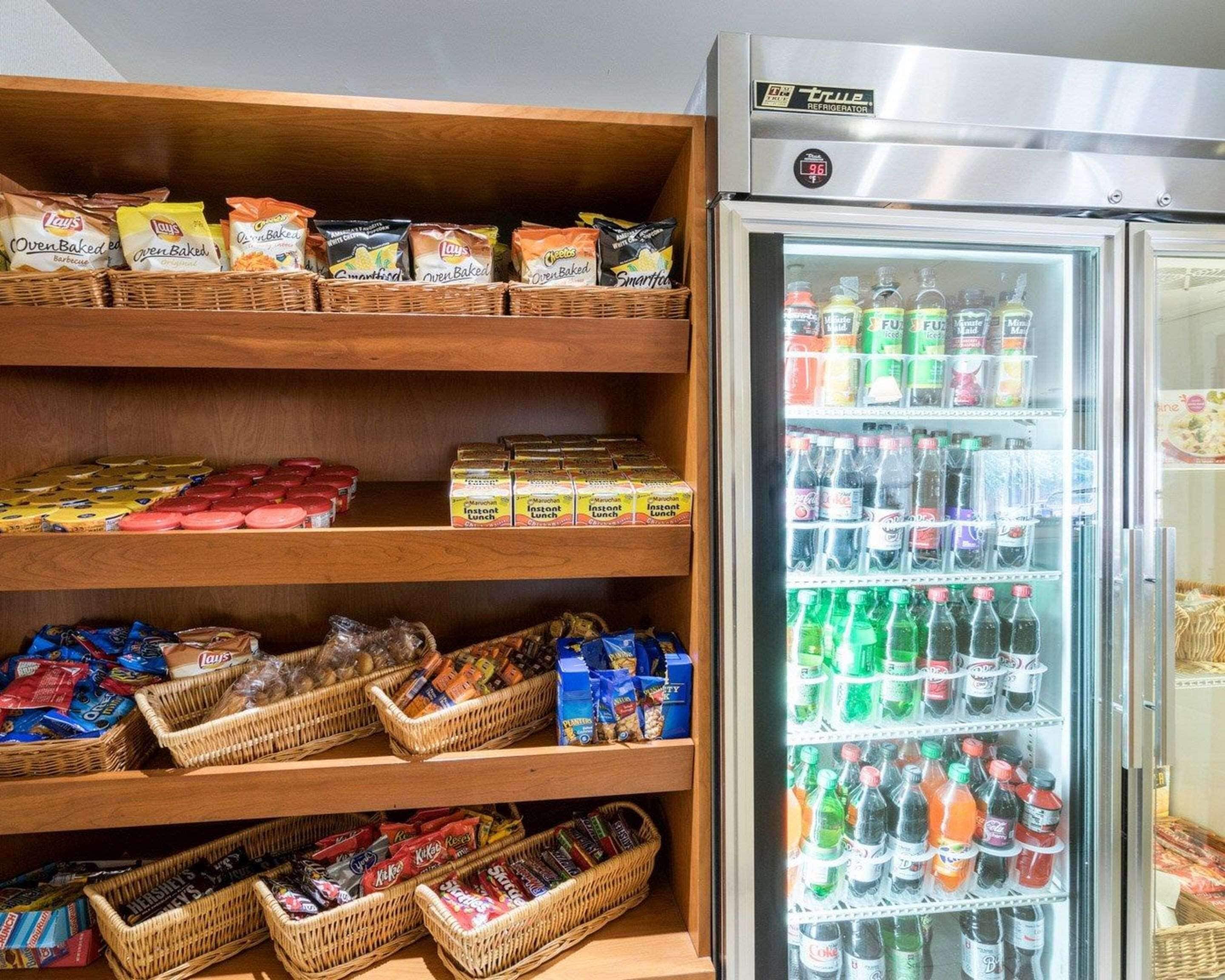 Zona de exhibición de bocadillos y bebidas con estantes llenos de diferentes opciones y un refrigerador con bebidas embotelladas.