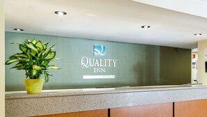 Un mostrador de recepción con una pared verde, una planta en maceta y un cartel de Quality Inn.