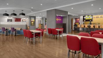 A modern dining area with red chairs and wooden tables, a counter with a coffee machine, and a wall with a 'Coffee' sign.