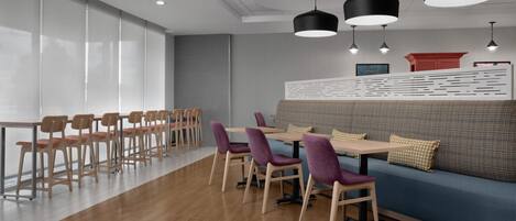 A modern dining area with wooden tables and chairs, a blue sofa, and black pendant lights.
