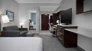 Una habitación de hotel moderna con una cama, un escritorio con computadora, un televisor y una lámpara.