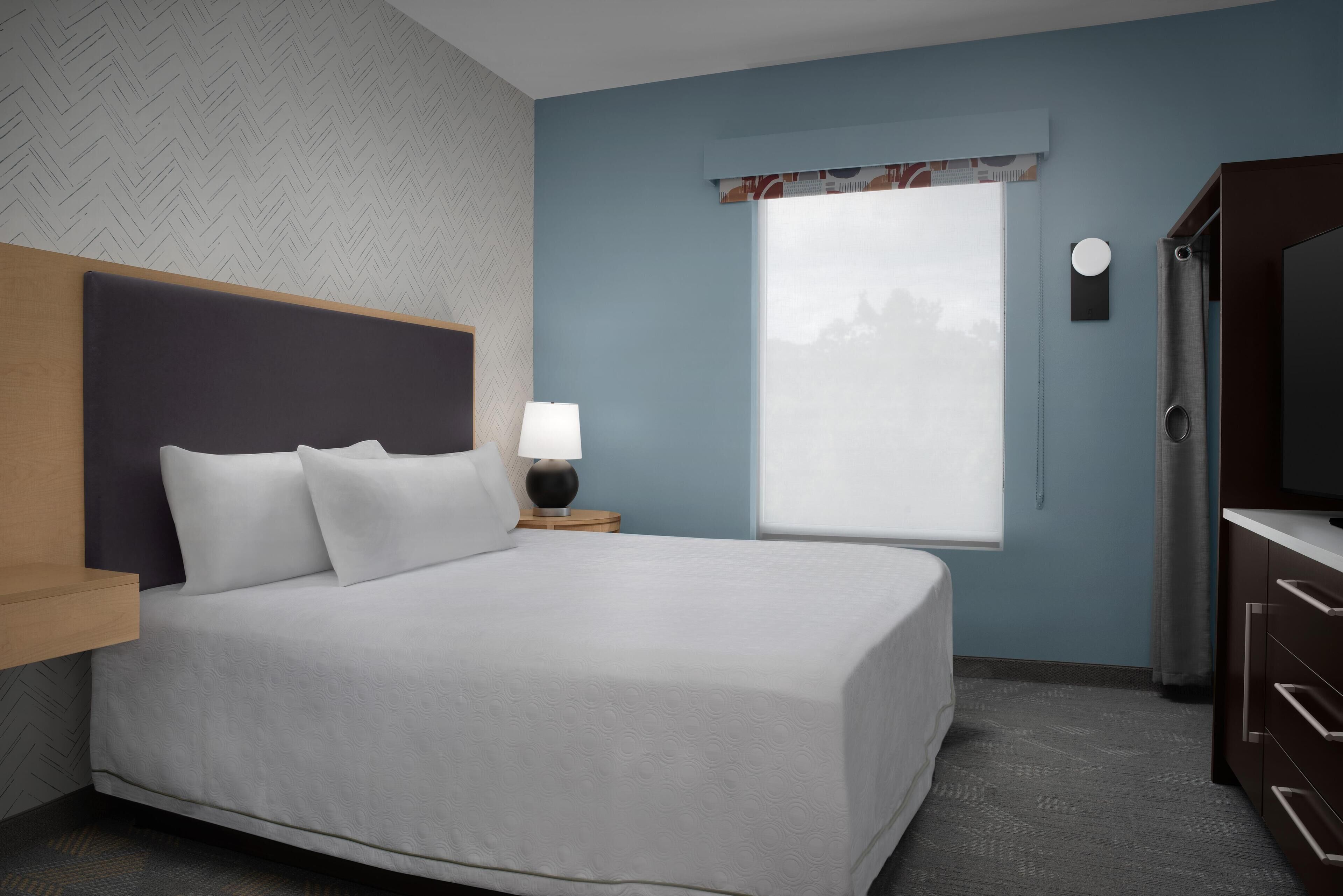 Une chambre d’hôtel bien aménagée, avec un grand lit, une table de chevet avec une lampe, une fenêtre donnant sur un beau paysage et un téléviseur posé sur un meuble.