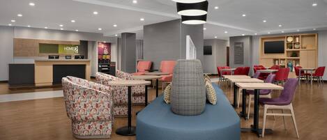 En moderne hotellobby med reception, siddeområder og et stort skærmbillede.
