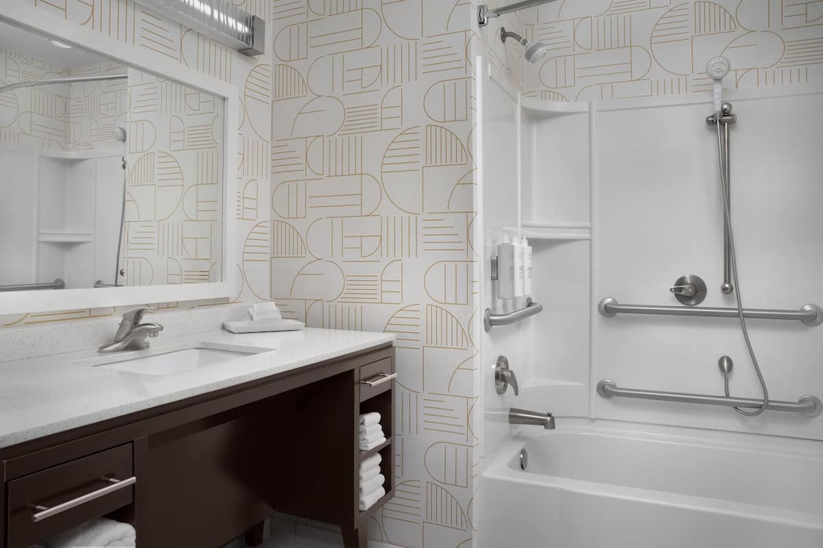 A modern bathroom with a white sink, dark wooden vanity, a large mirror, and a shower with a handheld showerhead.