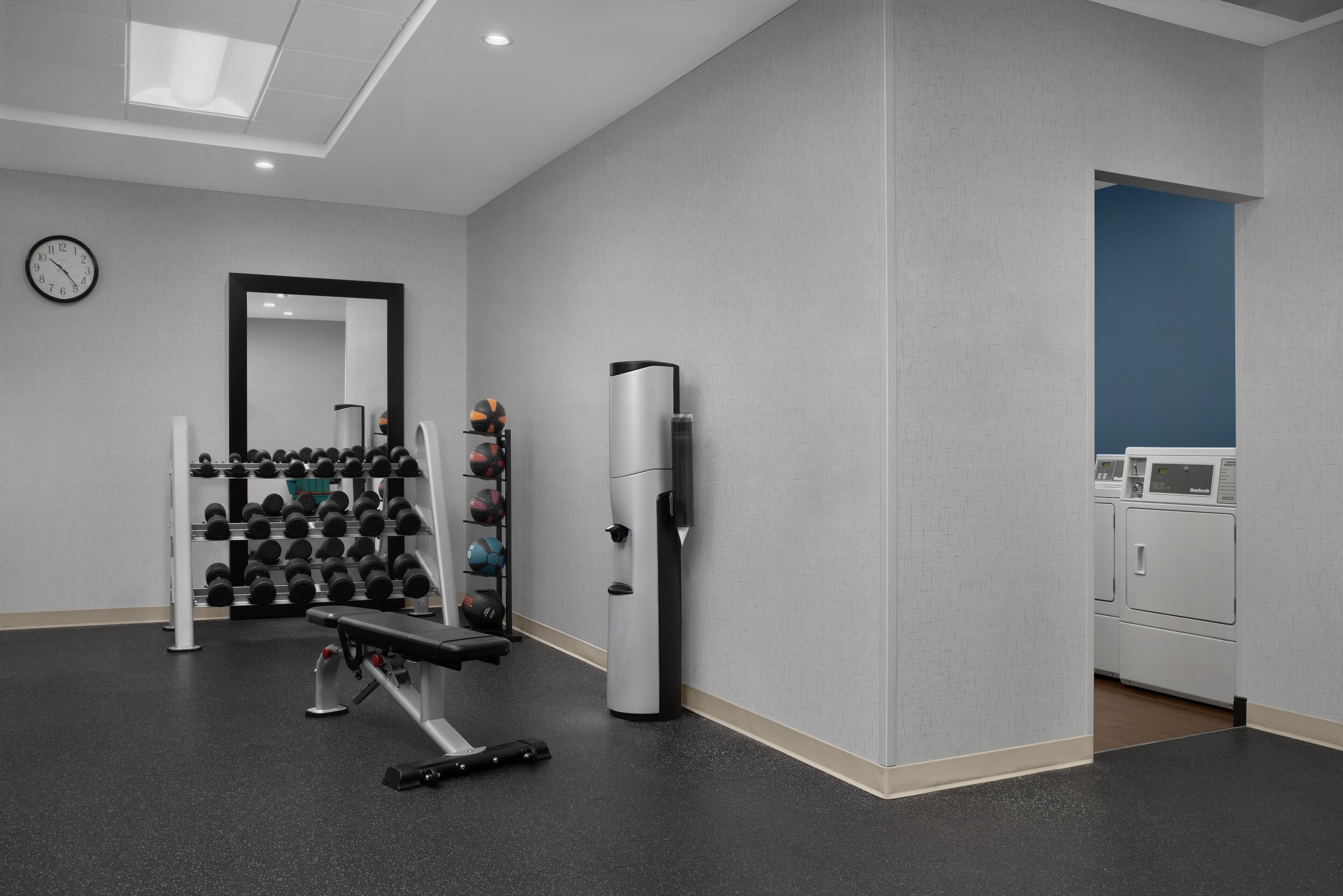 A gym with exercise equipment, a mirror, and a clock on the wall.