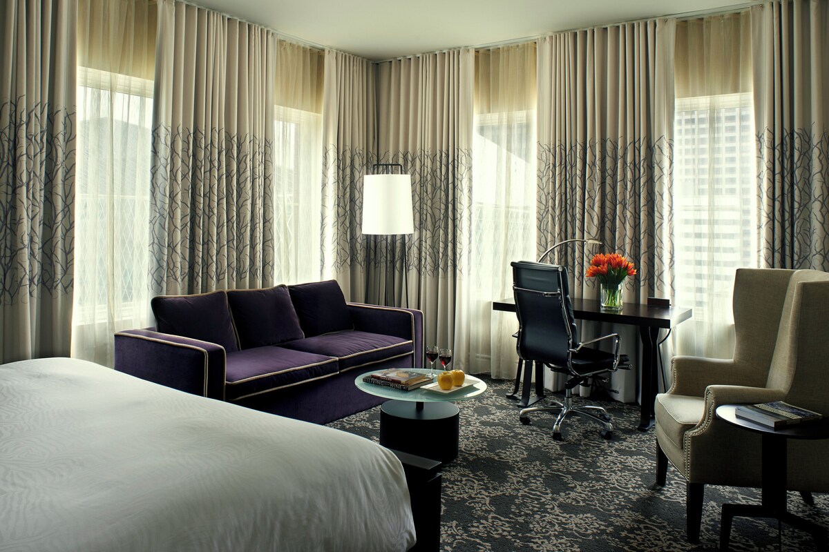 A hotel room with a bed, a sofa, a desk with a chair, a coffee table, and a lamp.
