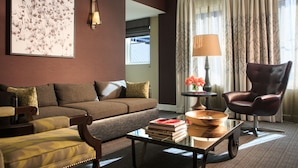 A living room with a brown sofa, a leather armchair, a coffee table with books, a lamp, and a vase with flowers. - Kimpton Hotel Vintage Seattle by IHG (Seattle)