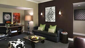 A modern living room with a dark green sofa, a black and white pouf, a coffee table with fruits, and artwork on the walls. - Kimpton Hotel Vintage Seattle by IHG (Seattle)