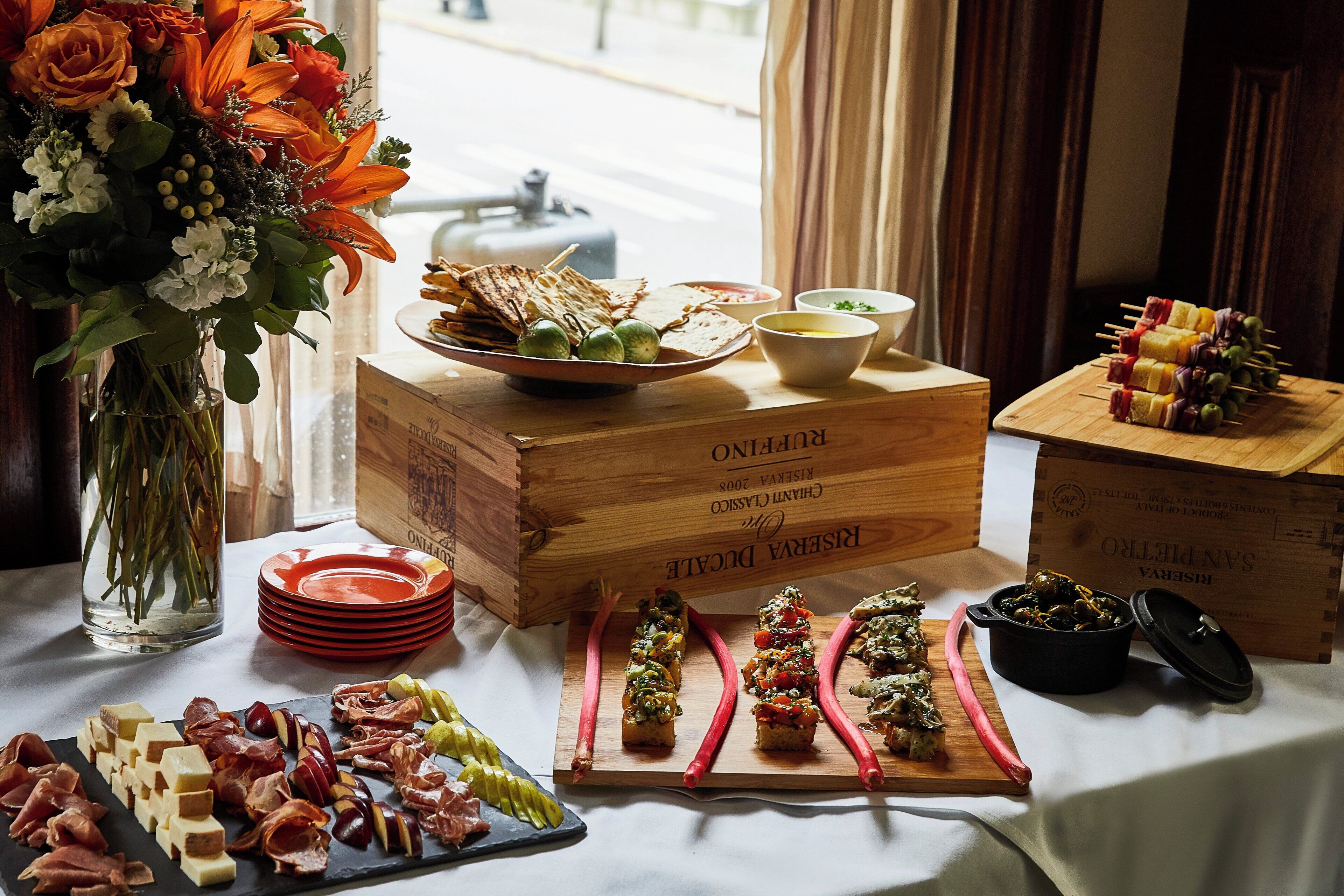 A table with various food items, including cheeses, meats, and vegetables, arranged on a wooden table with a white tablecloth.