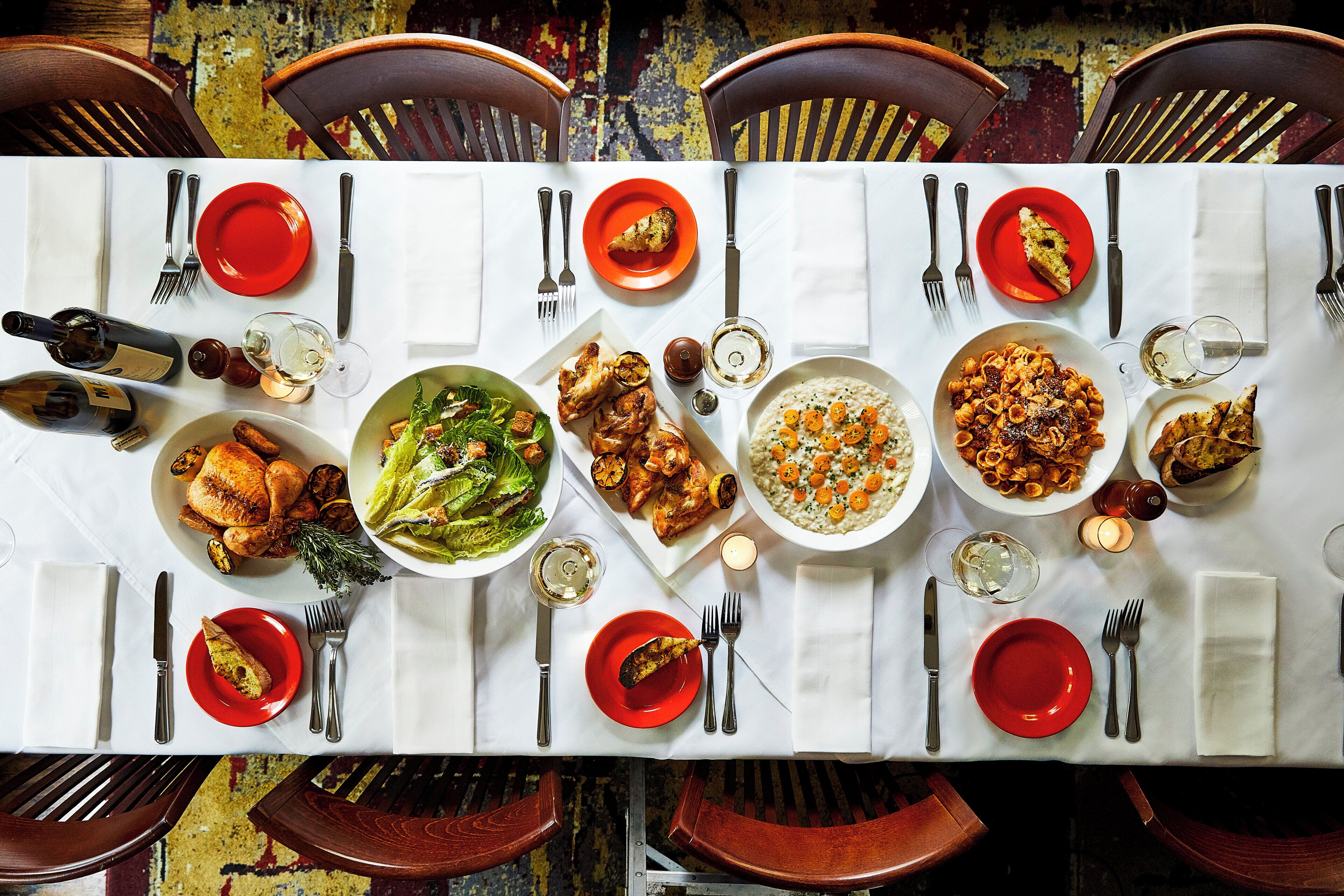 Une table à manger dressée pour un repas, avec différents plats et des verres à vin.
