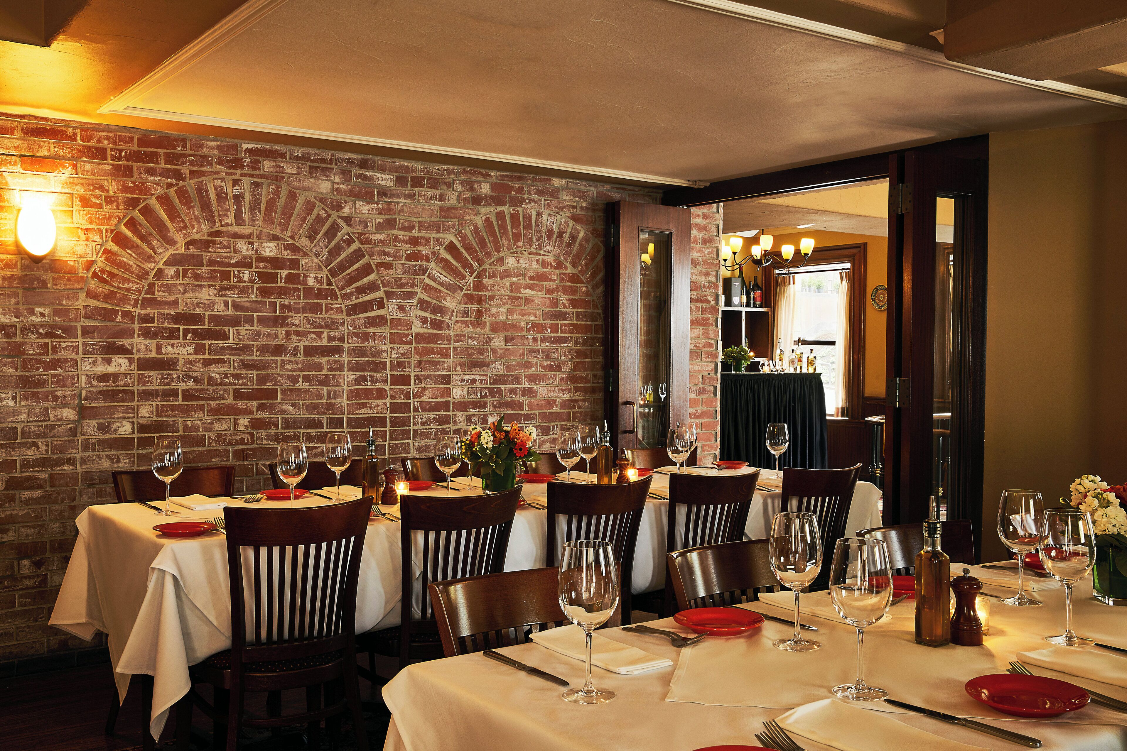 L’intérieur d’un restaurant avec des murs en briques, de nombreuses tables dressées pour le service et une lumière douce et chaleureuse.