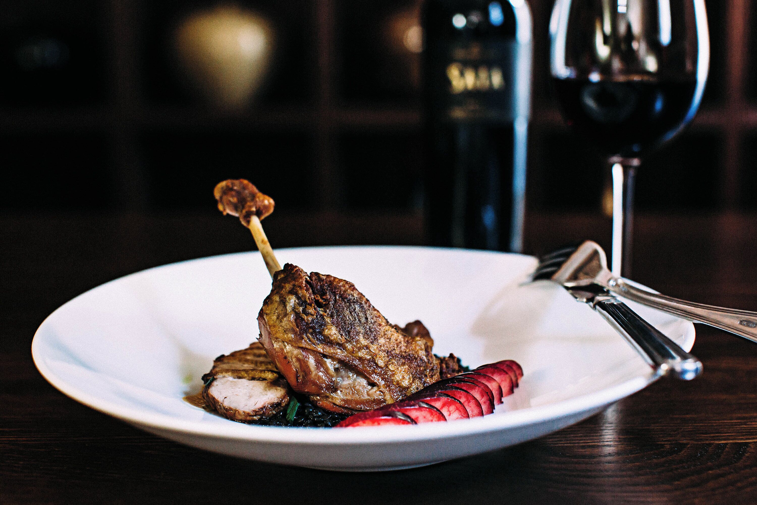Un plato con un guiso de carne, una copa de vino tinto y un tenedor sobre una mesa de madera.