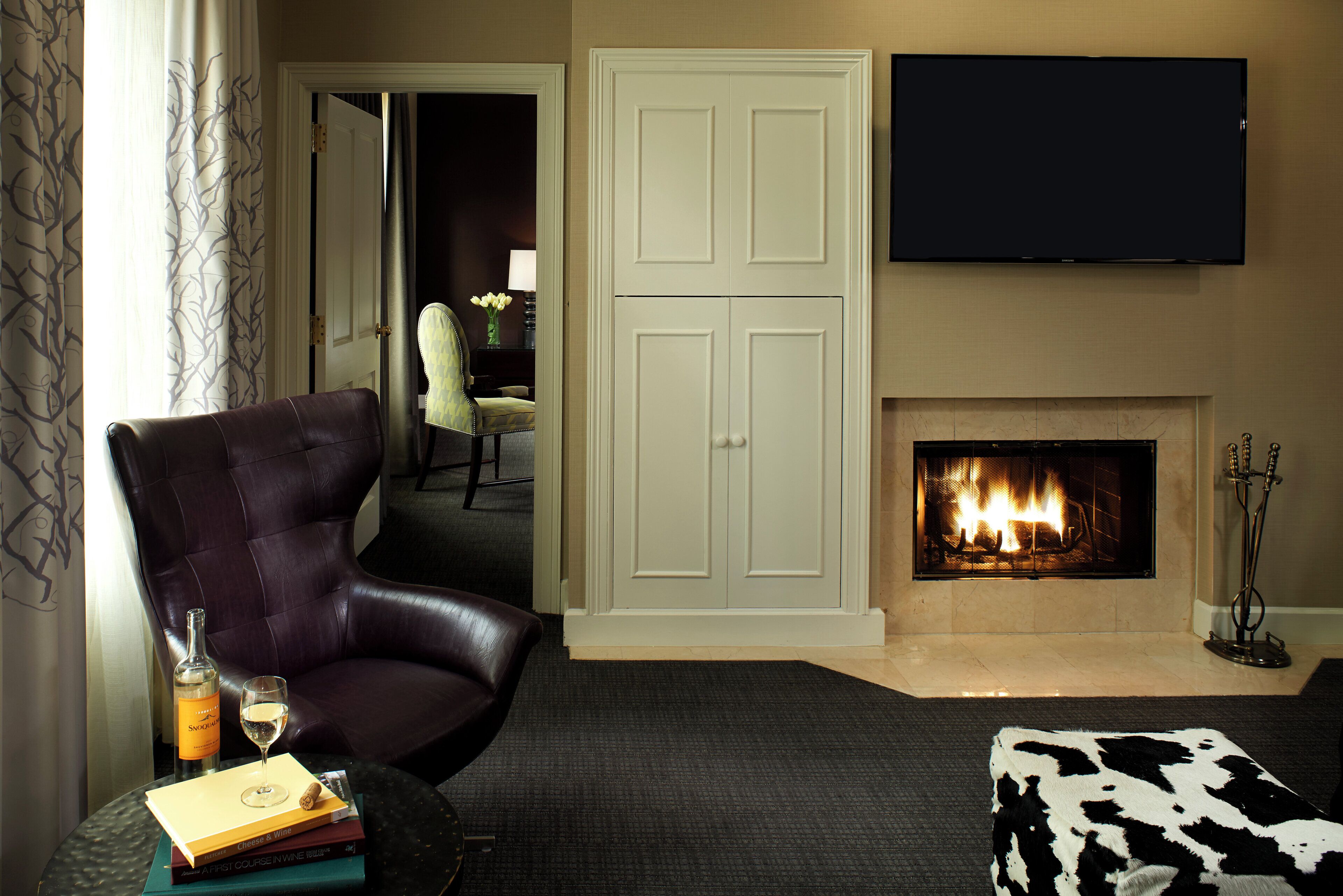 A living room with a leather armchair, a fireplace, a flat-screen TV, and a dining area in the background.