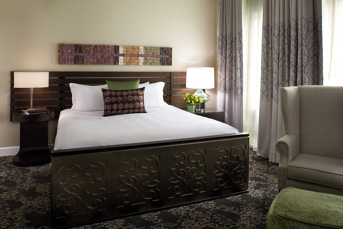A hotel room with a large bed, two bedside tables, a chair, and a decorative wall piece.