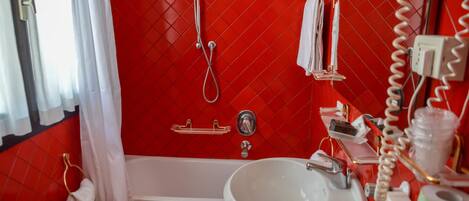 A bathroom with a red tiled wall, a white bathtub, two sinks, a showerhead, and a towel rack.