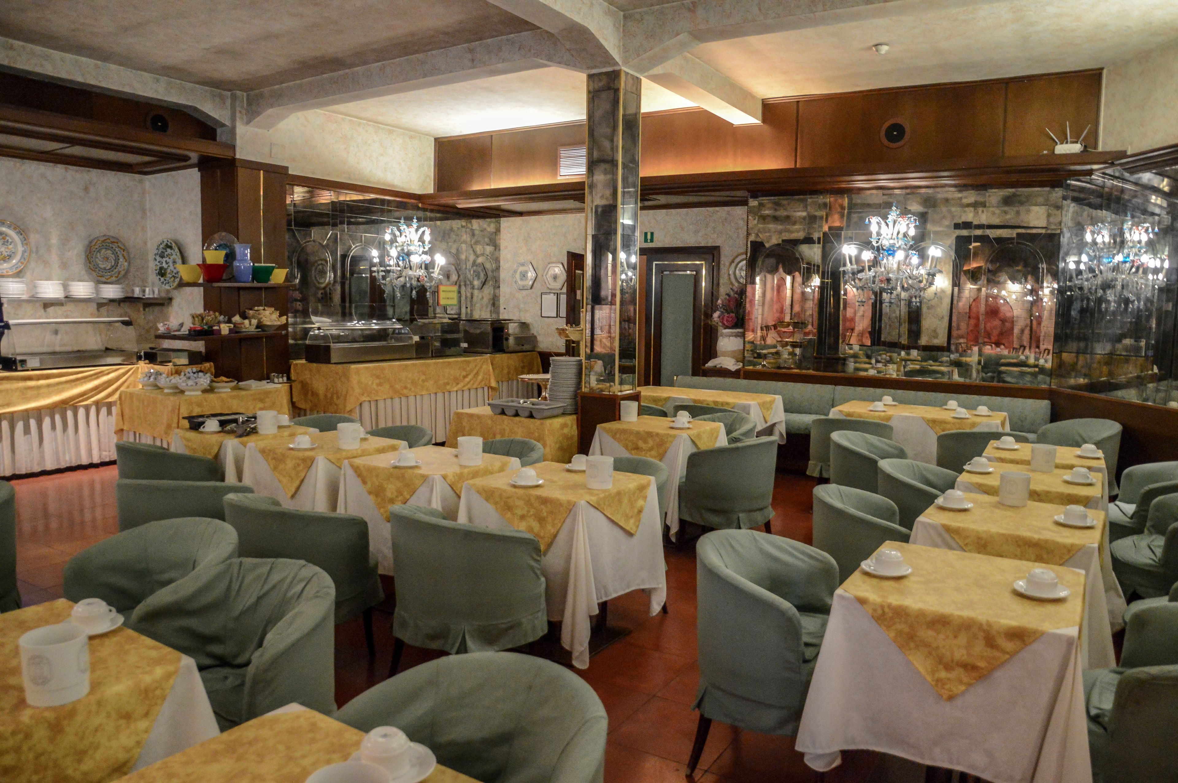 A restaurant with multiple tables and chairs, a buffet area, and a decorative mirror.